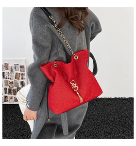 Detail of red textured leather bucket bag featuring gold S-logo, tassels and chain strap