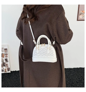 White shell-shaped handbag featuring intricate geometric embroidery and golden zippers