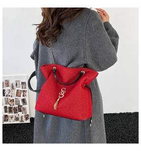 Détail du sac cabas rouge texturé avec logo SS doré, pompon et bandoulière chaîne