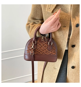 Detail of dark brown shell bag featuring intricate woven leather and crown emblem