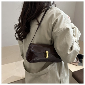 Deep brown patent leather baguette bag with gold buckle shown on a model's shoulder