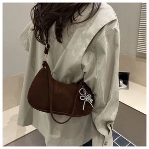 Détail d'un sac hobo en daim marron foncé avec un pendentif nœud en perles argentées