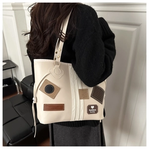 Detail view of cream tote bag featuring fashion patches and vertical decorative straps