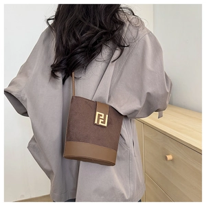 Detail of brown leather bucket bag featuring a gold geometric metal buckle on the side