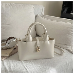 Borsa a secchiello minimalista in pelle bianco crema con ciondolo d'oro sul divano