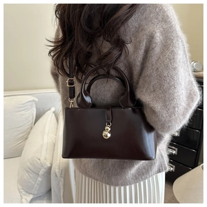 Detail of dark brown tote bag with gold ball charm on a model in home setting