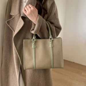Green and beige woven tote bag with silver rivets and top handles shown with a stylish coat