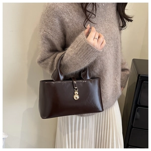 Detailed view of brown patent leather handbag with a gold sphere charm and unique handle
