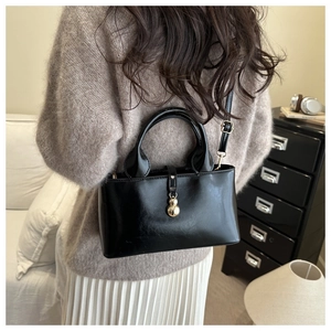 Close-up of black glossy handbag featuring a unique gold gourd-shaped metal pendant charm