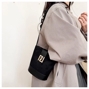 Detail of a black bucket bag featuring a gold geometric clasp worn with a beige trench coat