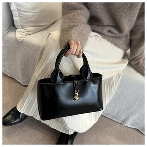 Close-up of black handbag featuring a smooth texture and a gold gourd-shaped pendant