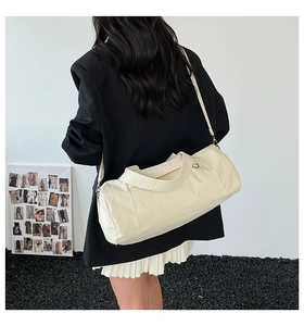 Detailed side view of off-white cylinder gym bag with adjustable strap on a shoulder