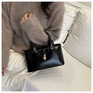 Close-up of black glossy handbag with a gold sphere pendant held against a white sofa