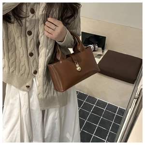Glossy brown patent leather bucket bag with gold pendant held by model in casual setting