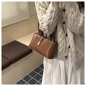 Detail of a brown leather bucket bag with a gold gourd pendant against a knit cardigan