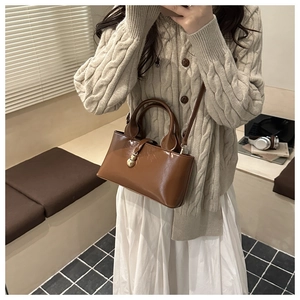 Detail view of deep brown glossy leather handbag with distinctive gold twin sphere charm