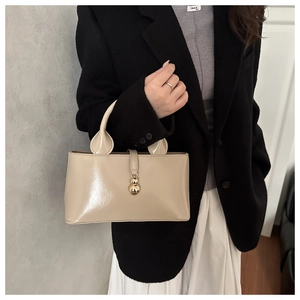 Detailed view of beige faux leather shoulder bag with gold gourd-shaped pendant on a model