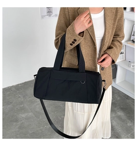 Detail of minimalist black nylon cylinder bag with adjustable strap and metal D-ring
