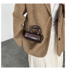 Fashionable cylinder bag with glossy dark red patent finish and golden chain shoulder strap