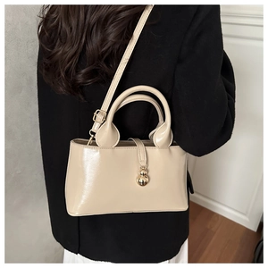 Detail of glossy beige patent leather handbag featuring exquisite gold gourd pendant charm