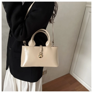 Detail of a beige baguette bag with a glossy finish and a gold spherical metal clasp