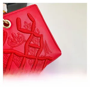 Detailed embroidery on red leather bag with gold hardware and floral silk ribbon