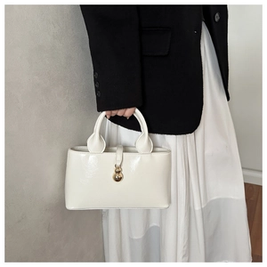 Minimalist beige glossy faux leather handbag held by model in professional suit outfit