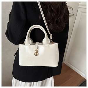 Glossy white bucket bag with gold metal pendant shown as a stylish crossbody accessory