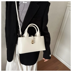 Close-up of the cream bucket bag featuring glossy finish and a golden spherical clasp