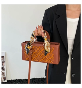 Detailed embroidery with crown motif and decorative silk scarf on brown handbag handle