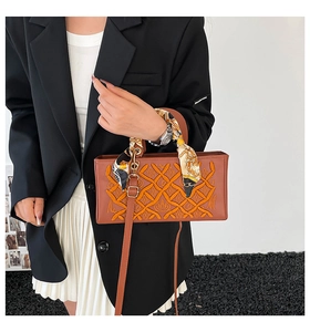 Detail of brown quilted embroidery handbag with decorative silk scarf and gold hardware