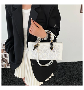 Close-up of white handbag with embroidered texture and silk scarf wrapped handle