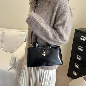 Glossy black leather bucket bag with gold ball clasp shown on a model in a warm home setting