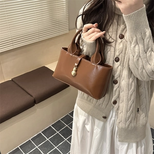 Chic brown glossy bucket bag with gold gourd charm held by a model in casual setting