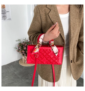 Close-up of red quilted handbag with heavy embroidery, silk scarf handle, and metal logo