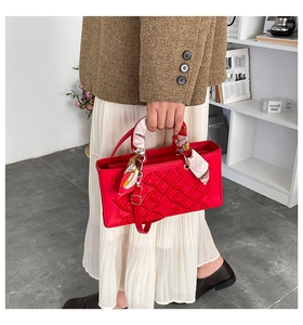 Detail of red quilted handbag with embossed patterns and a decorative silk scarf handle
