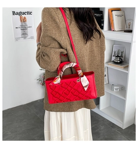 Detail of red quilted handbag with decorative silk scarf handle on model in modern setting