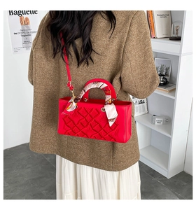 Detail of red quilted handbag with silk scarf wrapped handle and gold metal ring link