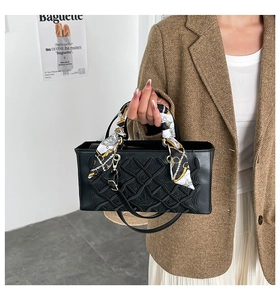 Detail of black rectangular handbag with embossed texture and patterned silk scarf handle
