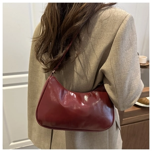 Detail of burgundy hobo bag in glossy leather worn by a model in a minimal room