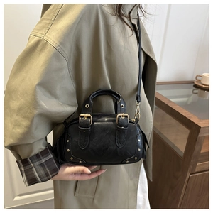 Detail of a vintage black mini Boston bag with gold buckle and rivets on a beige coat