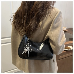 Detail of a shiny black faux leather hobo bag featuring a silver butterfly heart charm