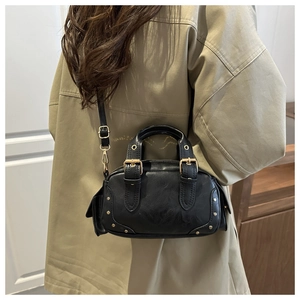 Detail of a vintage-style black mini moto bag with gold rivets and handle on a model