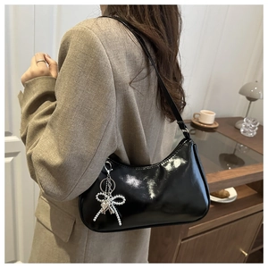 Detail of glossy black shoulder bag with silver bow pendant shown on model in a suit