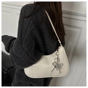 Detail of cream leather baguette bag with silver bow tassel worn on a grey sweater