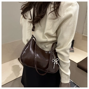 Detail of dark brown glossy underarm bag with silver bow pendant and adjustable strap