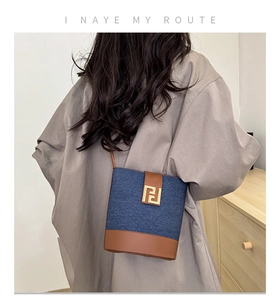 Detail view of a retro denim bucket bag with brown leather accents and gold buckle