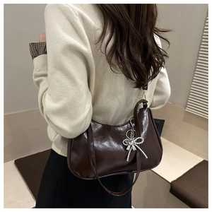 Detail of dark brown glossy underarm bag with silver heart bow charm and zipper closure