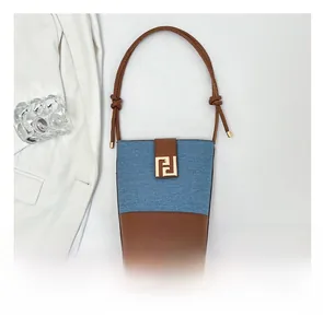 Detail of denim and brown leather bucket bag with gold metal clasp and thin strap