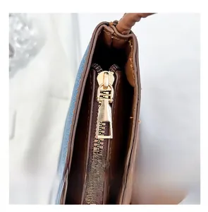 Close-up of golden metal zipper and blue denim stitching on brown leather bucket bag
